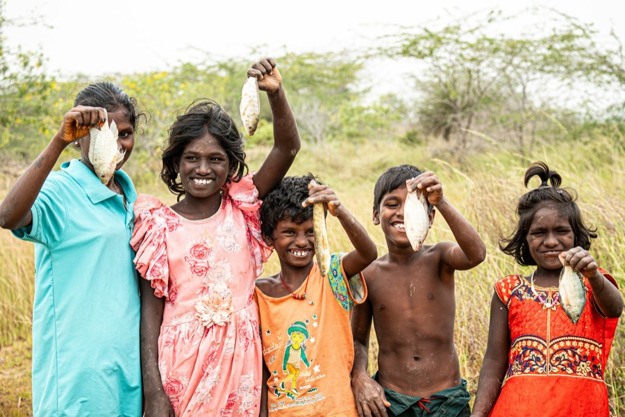 Children from a fishing village in Tamil Nadu smiling and holding up their catch