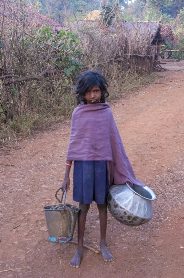 A young girl carrying water containers along a village road